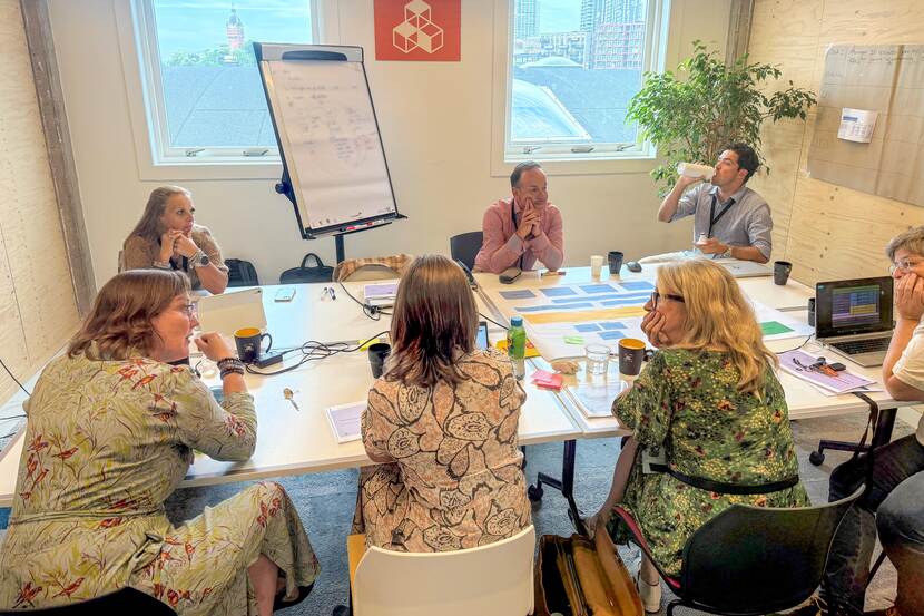 Aan een grote tafel zit een groep mensen. Zij overleggen en brainstormen.